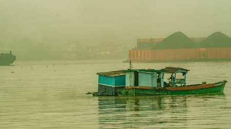 Sand miner activity at Mahakam River, Samarinda in the morning. Wooden boat take up the sand from the bottow of Mahakam River in the morning with barge of coal in the background.の写真素材