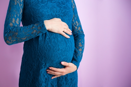 The tummy of a pregnant woman in navy-blue dress, while she is stroking itの写真素材