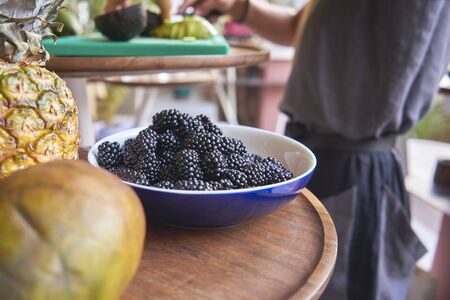 juicy, tasty blackberry in a ceramic plate, in the background a woman is cooking