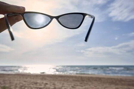 Male hand holds sunglasses on the background of the beach and sea