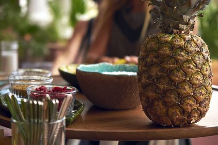 Pineapple stands on a table, along with ingredients for a smoothie bowlの写真素材
