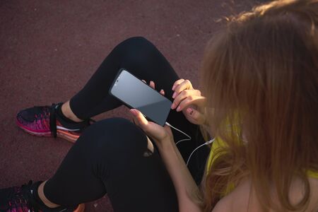 A woman is sitting on the playground and looking for something in the phone