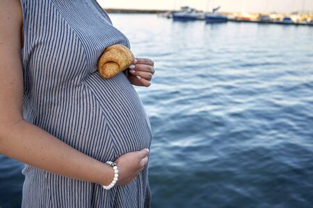 Pregnant woman holds croissant on her stomachの写真素材