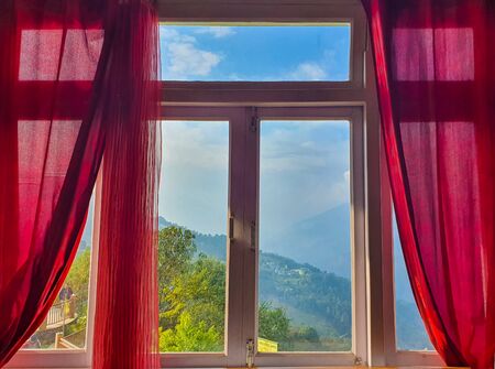 Window of a room with red curtains and a beautiful hill view in the backgroundの写真素材