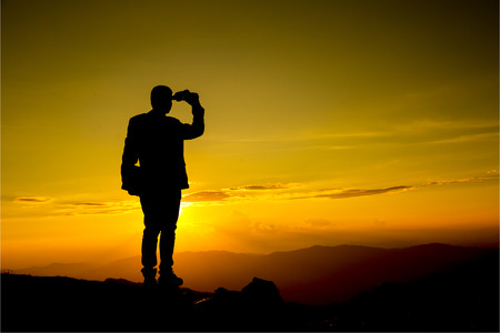 Businessman hold laptop and watch binoculars for his vision on the high mountainの写真素材