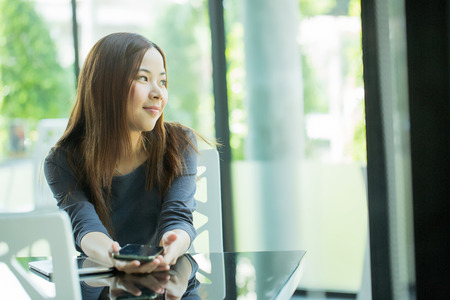 Young Asian girl use mobile phone for search information in coffee shopの写真素材