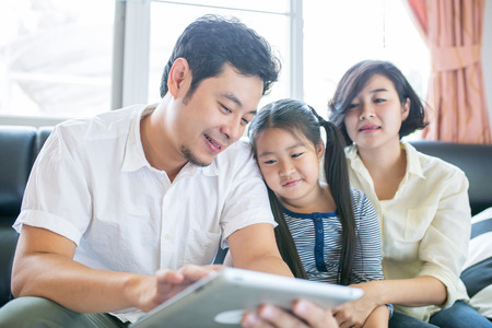 Asian family lifestyle. Father ,mother and daughter watch tablet for enjoy together in guest room.の写真素材