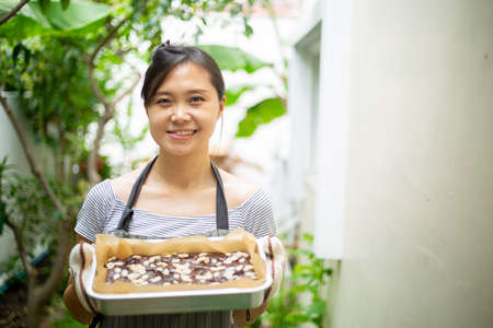 Chinese woman holding fresh brownies chocolate after finished cooking food.Asian girl holding sweet dessert for show her homemade at home.の写真素材