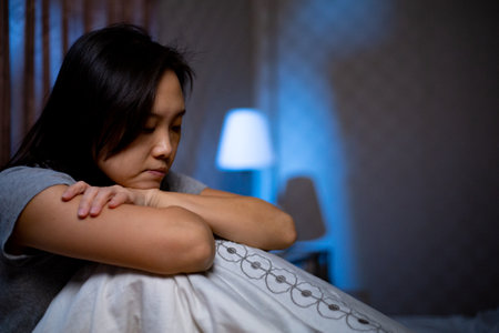 Depressed Asian woman can not sleep on the bed. Worry girl sitting and thinking her life in the bedroom.Sickness pain after headache and ill healthy.の写真素材
