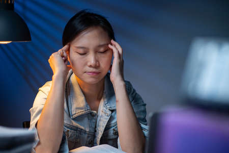 Asian woman writing documents in overtime at night.Working deadline in office.Officer girl headache...