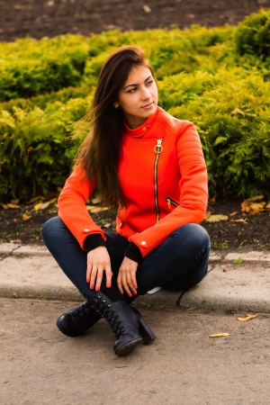 Young nice girl in vibrant orange jacket walking in autumn city の写真素材