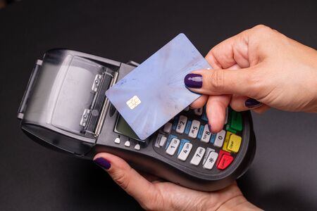 Female hand with credit card and bank terminal, Card machine or pos terminal with inserted credit card isolated on black backgroundの写真素材