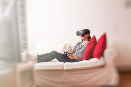 Casual young woman sitting on the sofa at home having fun playing a virtual reality video game