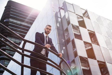 pensive businessman leaning on a rail and looking down at cameraの写真素材
