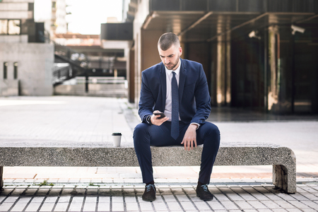 young businessman in suit using a smart phone outdoors, modern building on the backgroundの写真素材