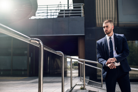 young confident businessman in suit standing outdoors and looking away, modern buildings on the backgroundの写真素材