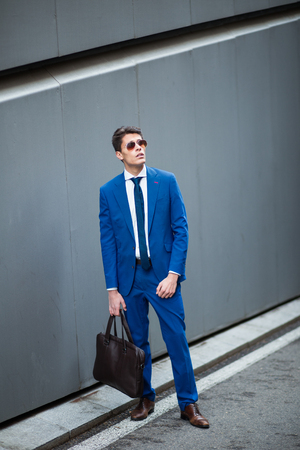 attractive young fashionable businessman standing in the street with a briefcaseの写真素材