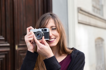portrait of an attractive young woman taking a picture with a vintage photo camera in the streetの写真素材