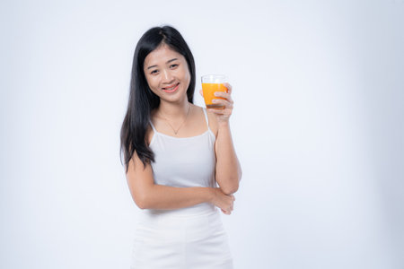 Portrait of a beautiful young asian woman drinking orange juice isolated on white backgroundの写真素材