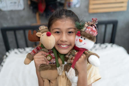 Sweet little girl is hugging a teddy bear, looking at camera and smiling while sitting on her bed at homeの写真素材