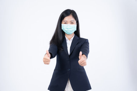 A confident beautiful young Asian business woman wearing green medical face mask and black suit, standing with her arms folded and looking at camera isolated on white background.の写真素材