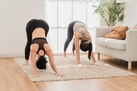 Two Asian women practicing yoga at home. They are standing in downward facing dog exercise.の写真素材