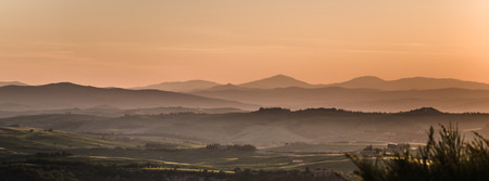 Panoramic view on fields in Tuscan landscape colored by the setting sun with clear silhouette of the mountains in the backgroundの写真素材