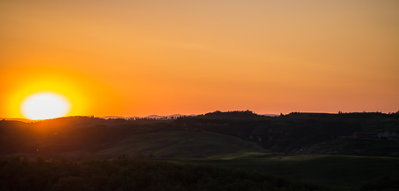 Panoramic view on Tuscan landscape colored by the setting sun with clear silhouettes of cypress trees and the mountains in the backgroundの写真素材