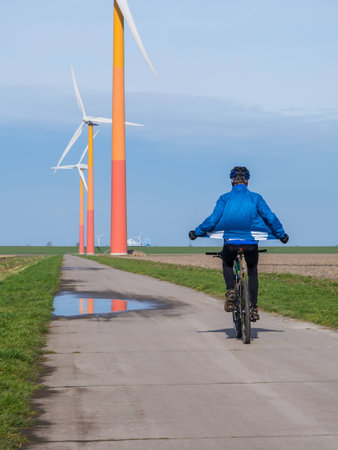 Mountain biker riding in the vicinity of a brighly colored wind turbine in Dutch landscapeの写真素材