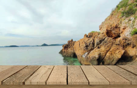 Wooden table top on blur sea  background with rock mountain.For montage product display or design key visual layout.View of copy space.の写真素材