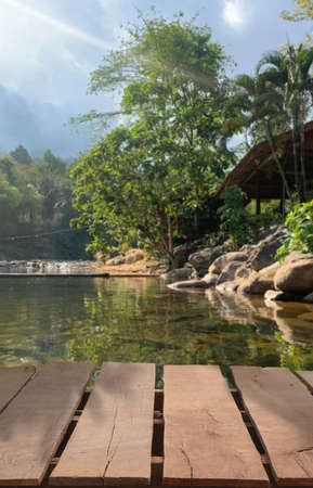 Wooden table top on blur stream water and forest natural background in private resort.For montage...