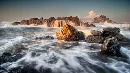 Beautiful seascape sunrise scenery with sea water flow and big rocks at Cibobos beach, Sawarna, Banten, Indonesia. Soft focus during long exposure shot.の写真素材
