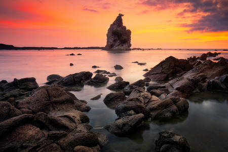 Beautiful seascape scenery of big boulder stone with small rock foreground during sunset at Tanjung Layar beach in Sawarna, Banten, Indonesia.Soft focus during long exposureの写真素材