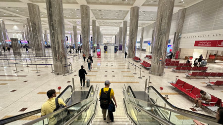 DUBAI,UNITED ARAB EMIRATES.15 SEPTEMBER 2023.Travelers descending on escalator in Dubai Airport, bustling with activityのeditorial素材