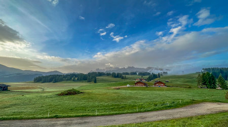 A verdant alpine pasture dotted with Italian houses, with the stunning Alpe di Siusi mountain ridge in the backdrop of the Dolomitesの写真素材