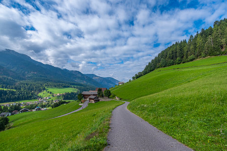 Santa Maddalena, Val di Funes, Quaint house along a winding road, framed by lush pastures, leading to the majesty of layered Dolomites, an enchanting Alpine tableauの写真素材