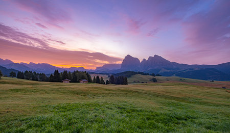 Alpe di Siusi, Italy, UNESCO Heritage, vibrant meadows, rustic huts. Charming alpine dwellings amid lush pastures frame the majestic backdrop of Alpe di Siusi.の写真素材
