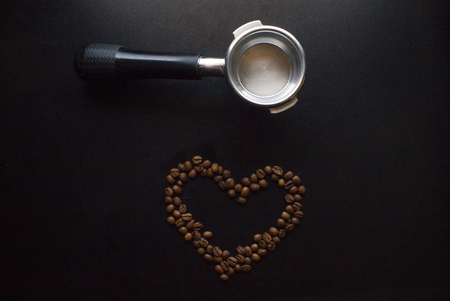 filter holder of espresso with scattered roasted coffee beans on black table background, top view.の写真素材