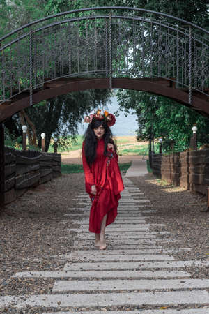 beautiful young girl in a red dress with long sleeves and a wreath is dancing under the bridge in the parkの写真素材