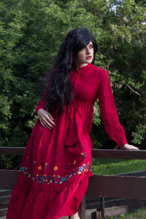 beautiful young girl in a red boho dress with long sleeves walks in the park on the bridgeの写真素材