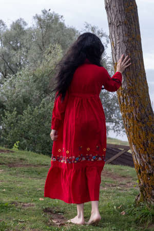 beautiful young girl in a red boho dress with long sleeves walks in the parkの写真素材