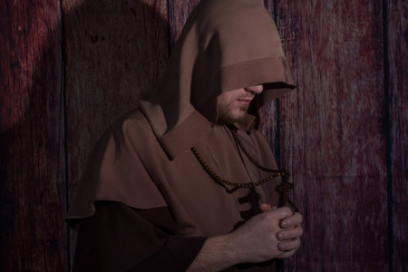 Medieval monk praying with closed eyes, with wooden cross in arms