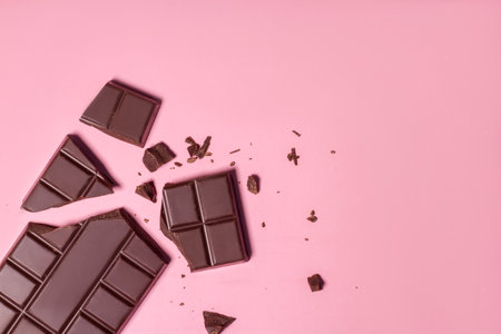 Broken pieces of dark chocolate on pink background. Top view.の写真素材