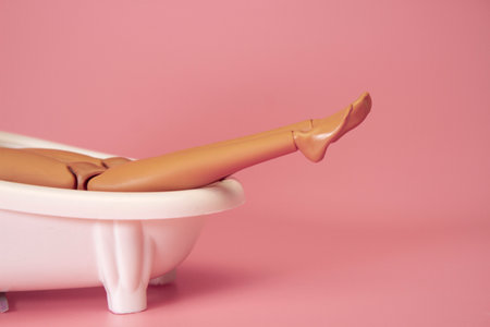 Doll bathing in a full bathtub on a pink background. Creative minimal beauty summer concept. Side viewの写真素材