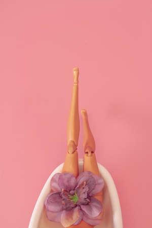 Doll bathing in a full bathtub on a pink background. Creative minimal beauty summer concept. Side...