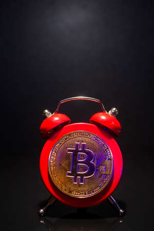 Bitcoin and alarm clock on black background. Deadline concept for investing in bitcoin cryptocurrency.の写真素材