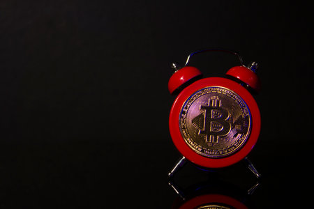 Bitcoin and alarm clock on black background. Deadline concept for investing in bitcoin cryptocurrency.の写真素材