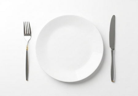 An overhead view of a pristine white plate, accompanied by a fork to the left and a knife to the right, suggesting a formal or simple meal setting.の素材