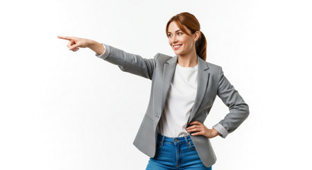A confident businesswoman in a grey blazer and jeans points to the left with her index finger, smiling. She is isolated on a plain white background.の素材