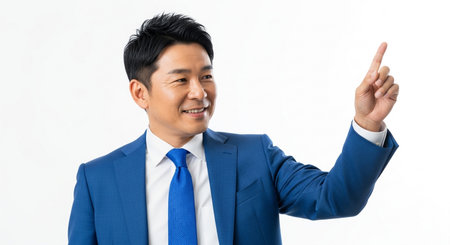 A confident Asian businessman in a sharp blue suit points upwards, suggesting a new direction, idea, or goal in a professional setting.の素材